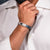 Man wearing a white shirt with rolled-up sleeves and a silver bracelet, against a dark textured background.